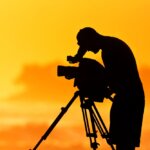 man uses video camera at sunset